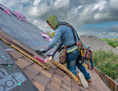 A roofing contractor installing shingles on a residential roof in a Texas neighborhood