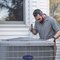An HVAC technician inspecting an outdoor condenser unit with a flashlight