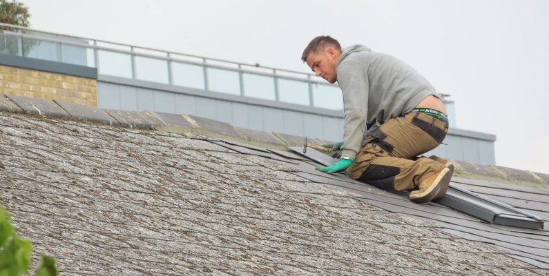 A roofing contractor laying shingles on a pitched roof