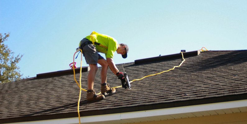 A roofer working on a pitched roof with a power drill