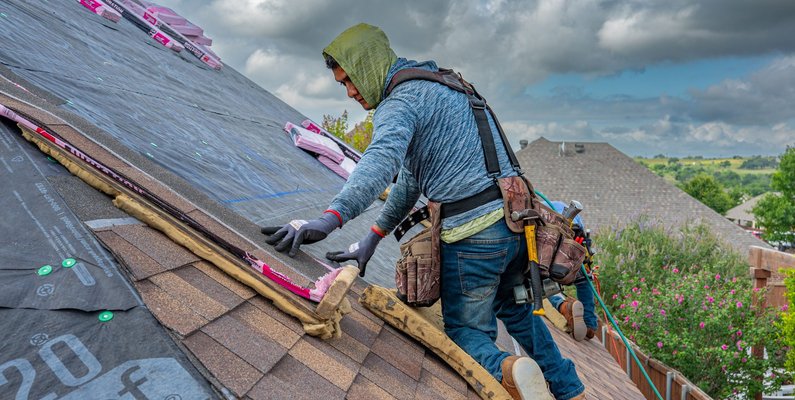 A roofing contractor installing shingles on a residential roof in a Texas neighborhood